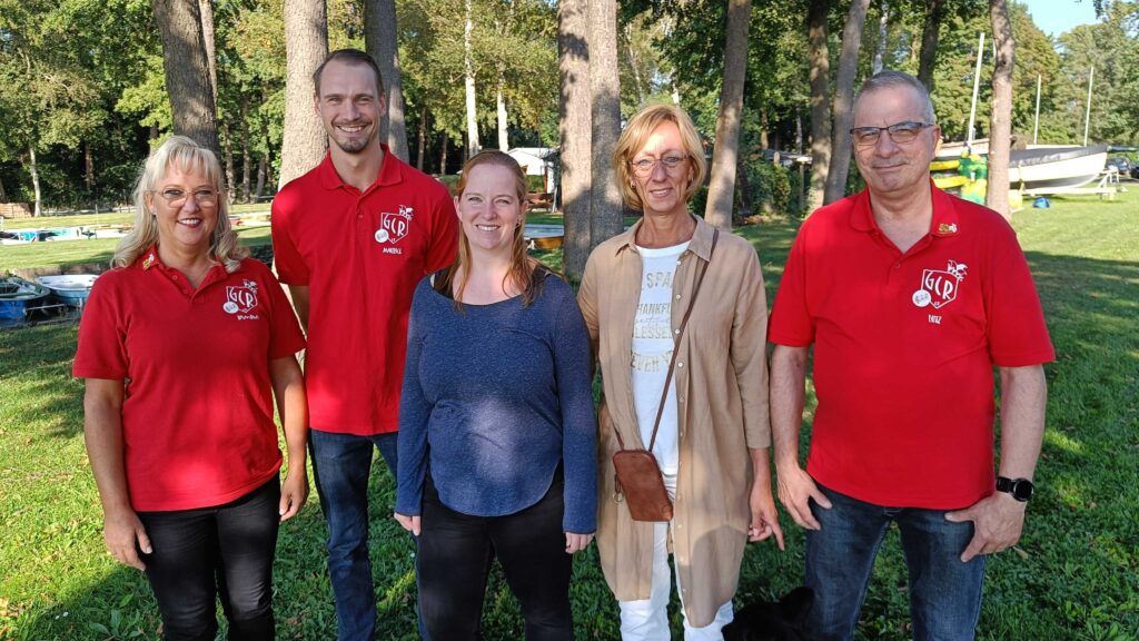 Drei Frauen und zwei Männer stehen auf einer Wiese und lächeln in die Kamera.